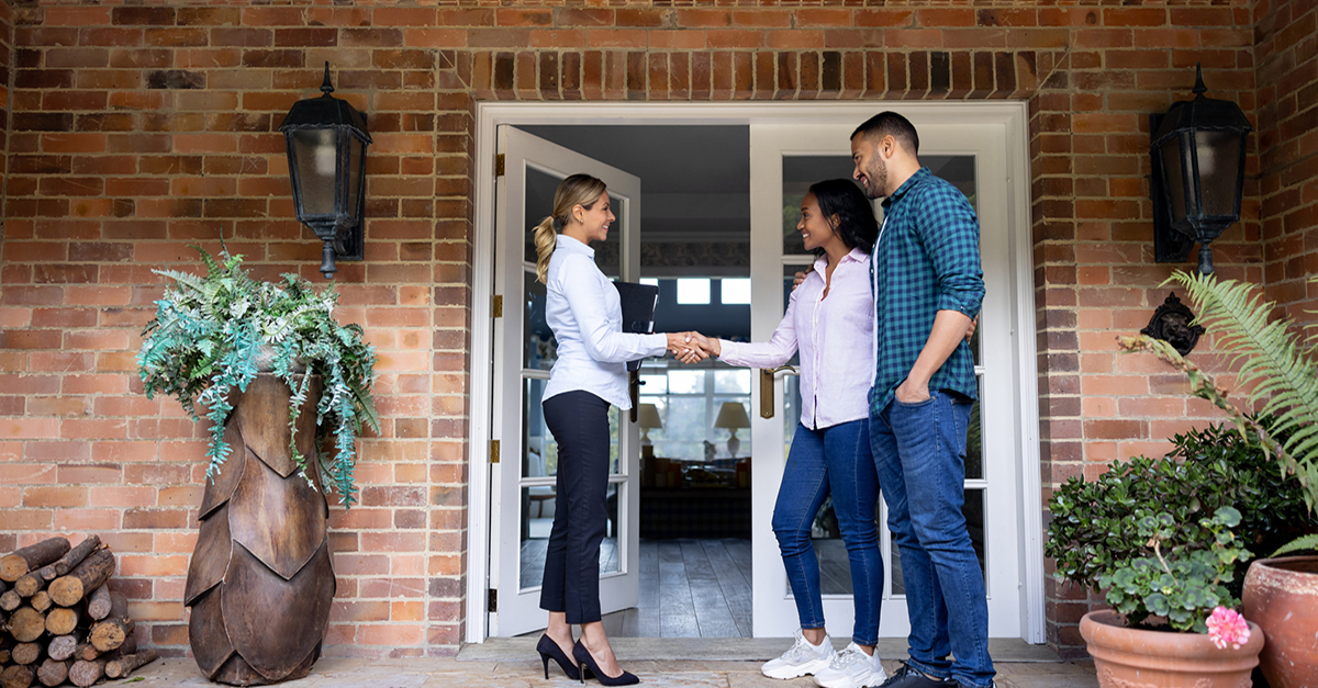 An agent shakes hands with clients outside a home